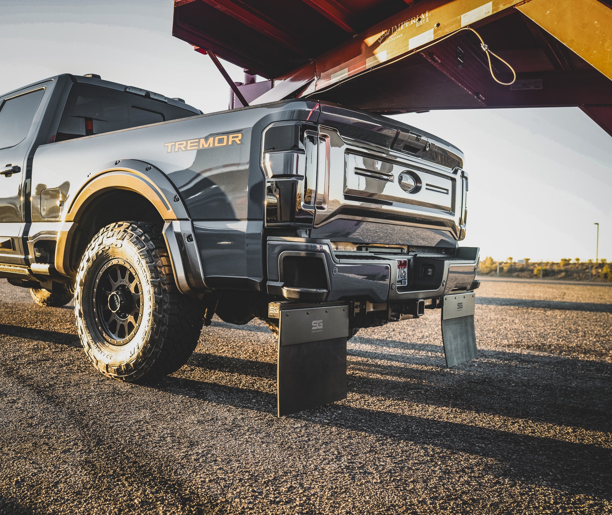Ford Super Duty single-wheel truck showing the Step N Guard step and mud flap system installed on the receiver hitch for towing.