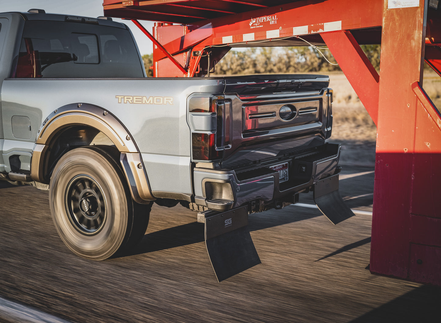 Action shot of the Step N Guard step and mud flap system successfully blocking rock spray and debris while the Ford Super Duty tows a trailer on a road.